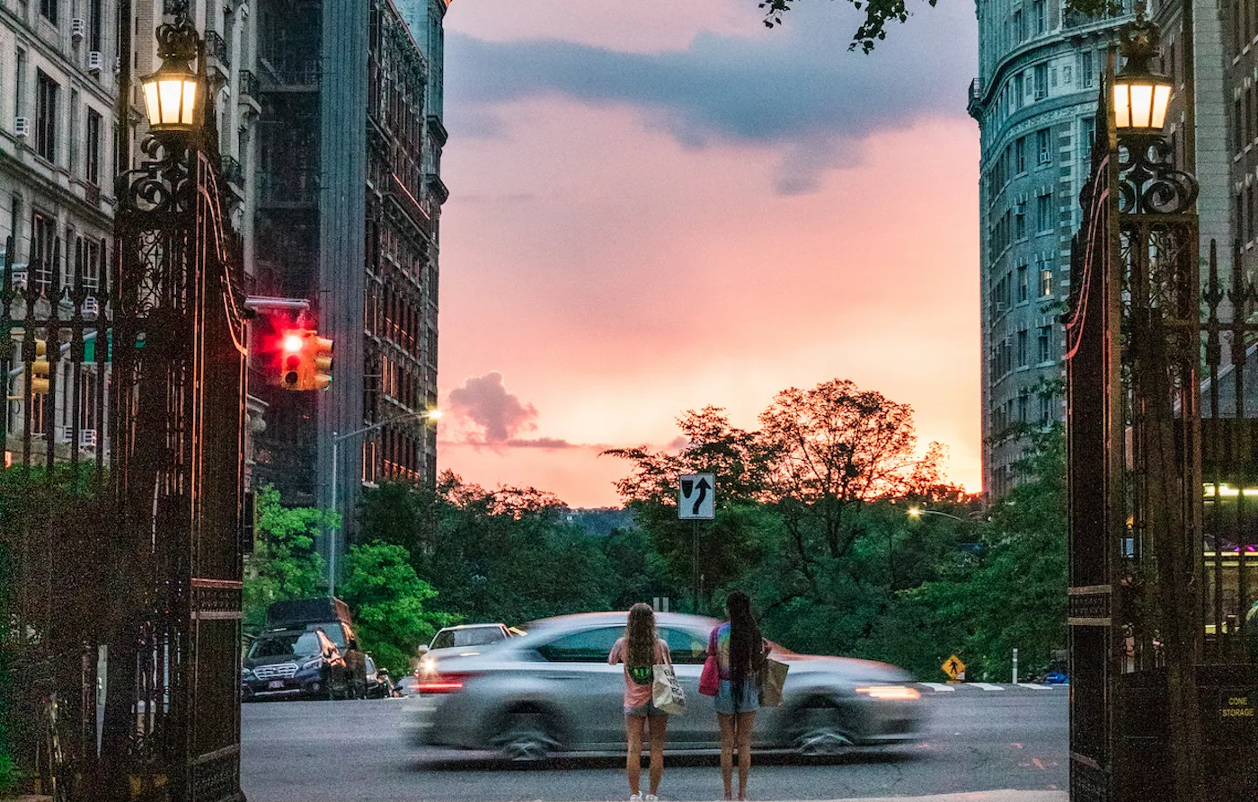 two students standing in front of the gates of Columbia University in front of a sunset