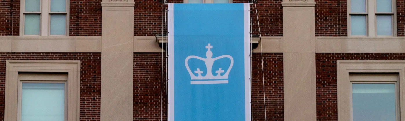 Photograph of a light blue Columbia flag in from of a brown building 