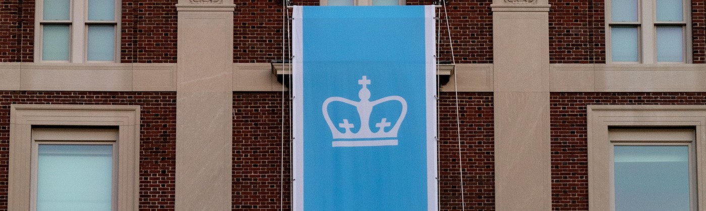 Photograph of a light blue Columbia flag in from of a brown building 