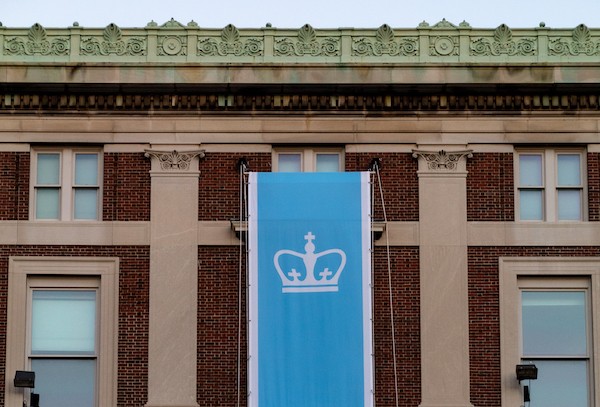 Image of a light blue Columbia University flag in front of a building 